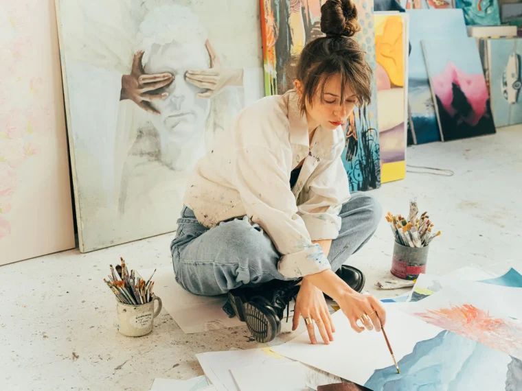 Artist at cluttered desk in sunlit room using 3D software animation bridging painting and modeling.